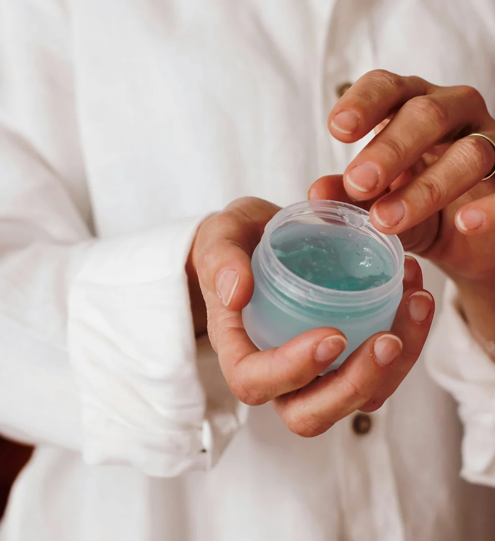 Persona con un camice bianco prende un po' di crema azzurra con una fresca consistenza in gel da un barattolo.