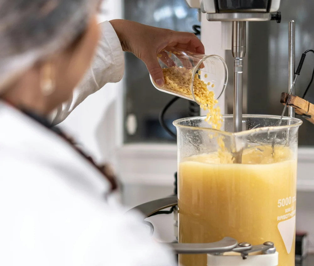 Un grosso beker di vetro trasparente graduato riempito con una sostanza gialla, posizionato sotto l'asta di un miscelatore meccanico da laboratorio