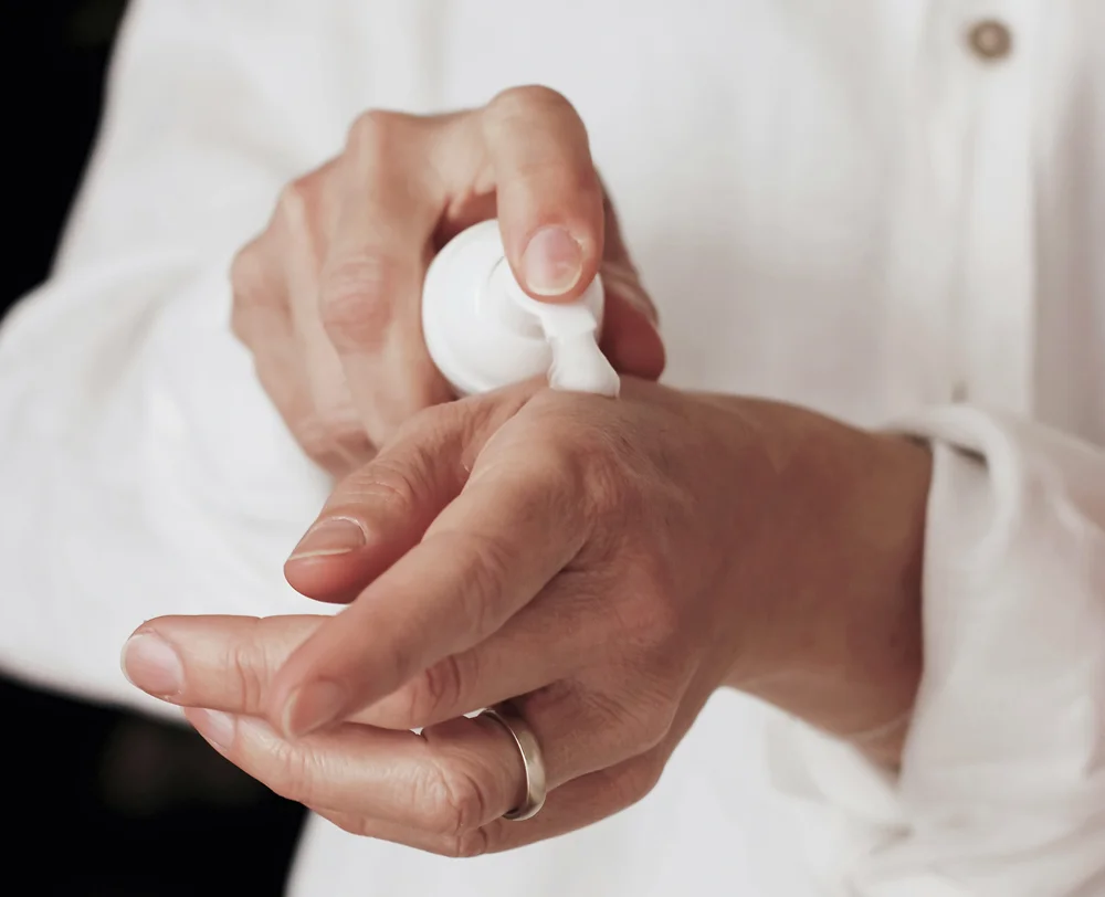 Una persona si mette la crema sulle mani premendo sulla parte alta del pack del prodotto.